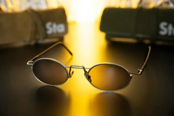 Close-up of sleek sunglasses on a shiny black surface with warm golden light.