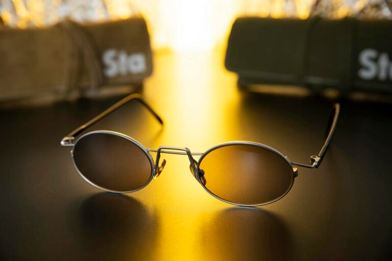 Close-up of sleek sunglasses on a shiny black surface with warm golden light.