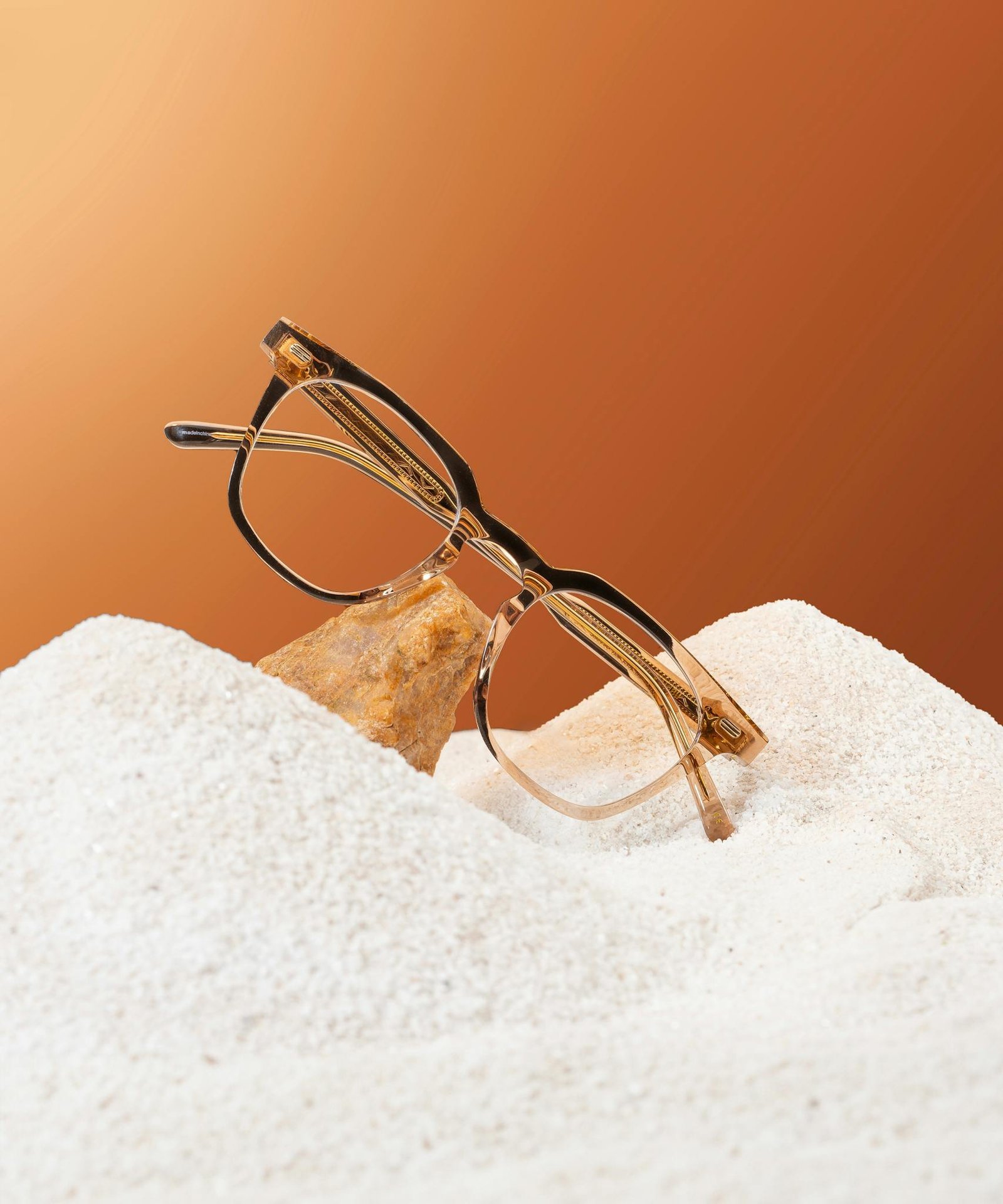 Elegant eyeglasses placed on a sandy surface with a gradient brown background, capturing modern style.