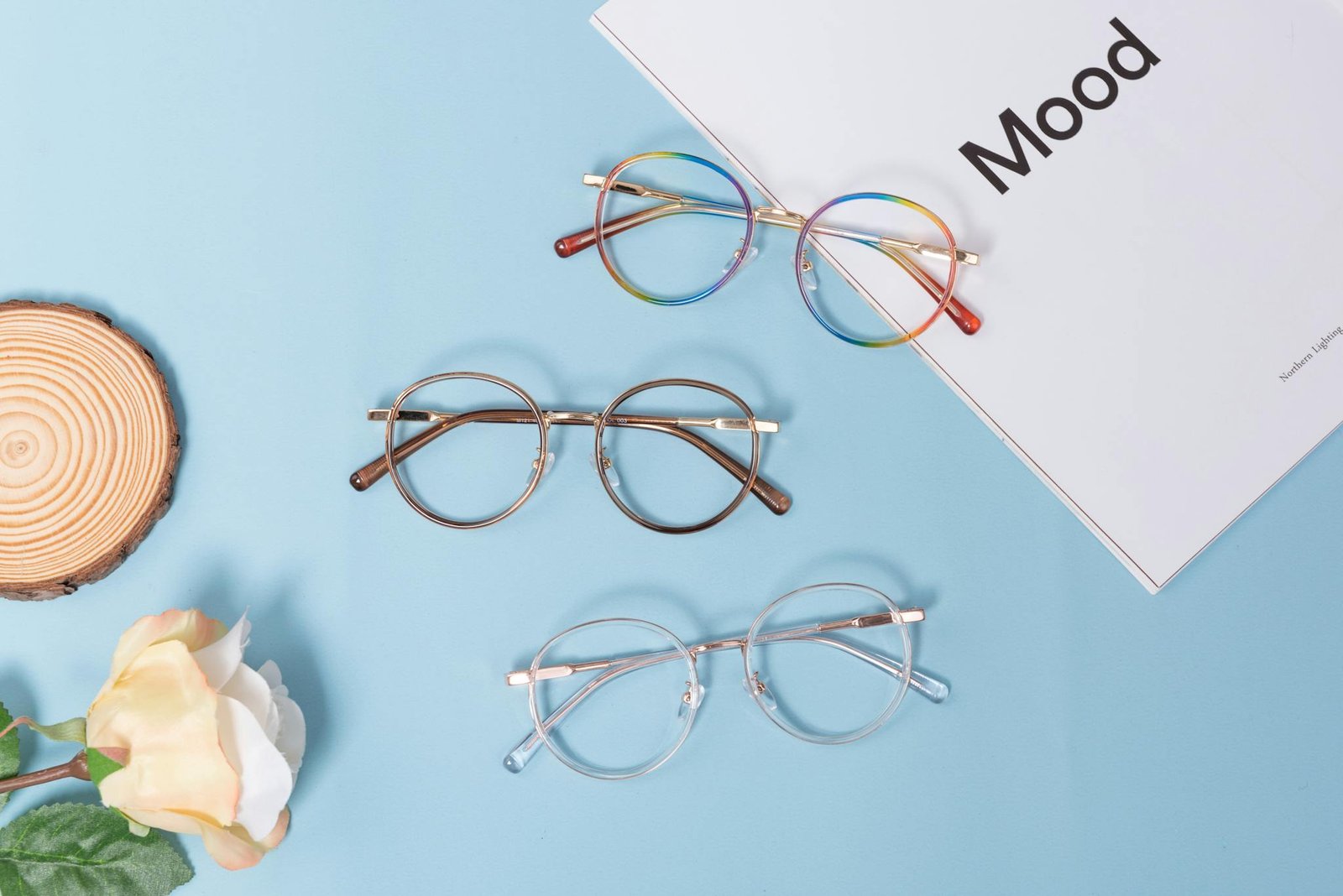 Flat lay of stylish eyeglasses and Mood magazine on a light blue backdrop.